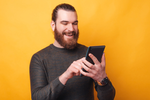 A joyful bearded man is talking with someone on his tablet being happy
