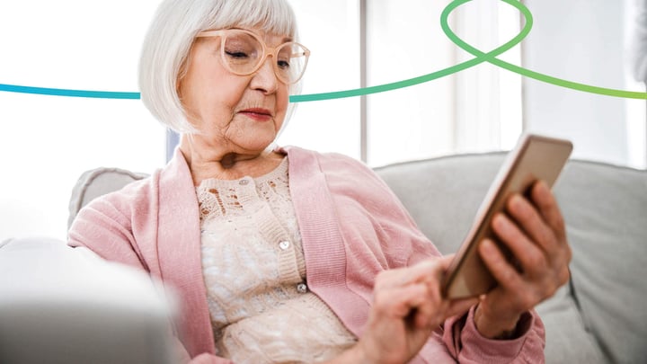 Elderly lady sitting on a sofa using a mobile phone.