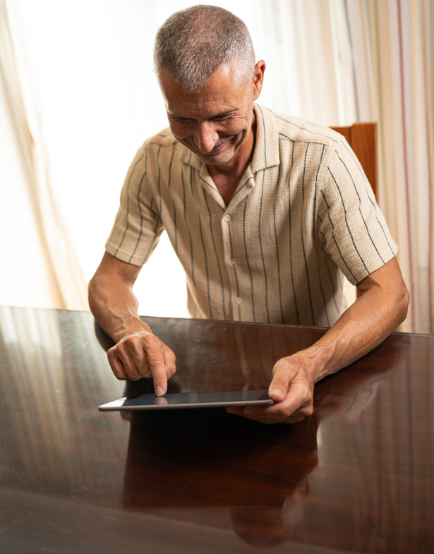 Middle-aged man sitting at a table holding a tablet device.