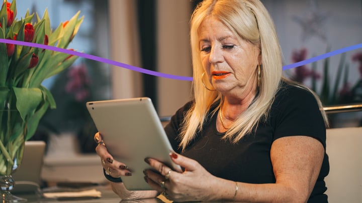 A 68 year old Caucasian woman sitting down and using a tablet device.