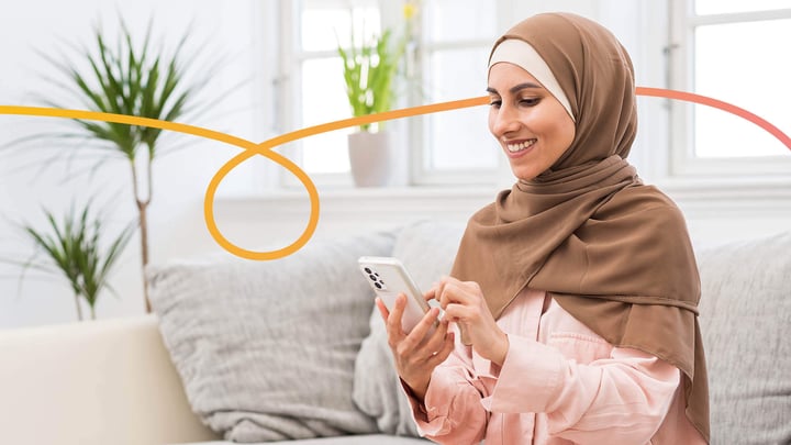 Young Muslim woman sitting on a sofa, using a mobile phone.