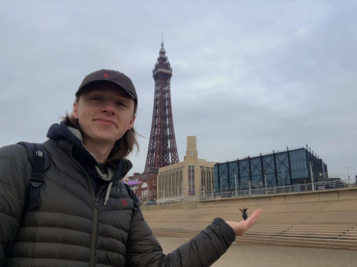 Young male in front of the Blackpool Tower posing with his hand flat with his friend in the background