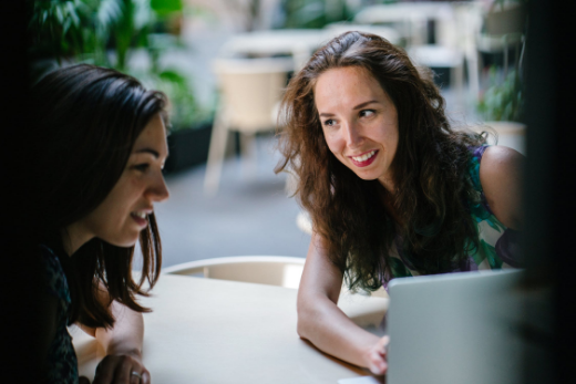 Two women sat at a table looking at a laptop