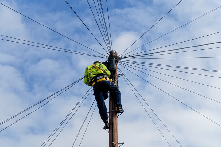 A Telecoms Operative climbing up a phone line in a safety harness and High vis jacket