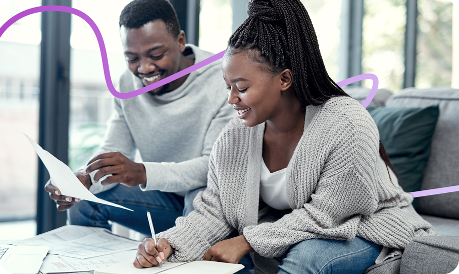 Couple doing finance planning, writing budget paperwork on sofa at home.